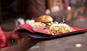 A server carries a tray with a burger, salad and side.