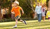 A young boy runs on the grass while his family looks on.