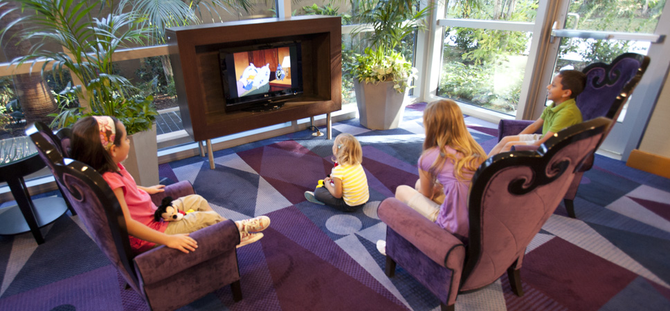4 kids are focused on a Disney cartoon in the TV viewing area of the Disneyland Hotel lobby.