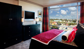 A flat-screen TV and large, black wardrobe and drawers face the plush bed.