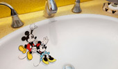 An image of Mickey has him holding the edge of the sink with one hand and, with the other, a dangling Minnie near the drain.