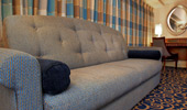 A Standard Room with long sofa, writing desk, chair and silver-framed mirror.