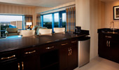 A wet bar, a refrigerator, dark wood cabinets and a view of Disneyland Resort from the living area of a 2-Bedroom Suite.