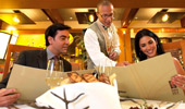 A couple seated at the table smiles while reviewing the menu and listening to the server answer their questions.