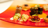 A bright orange plate contains small tastes of sushi and exquisite appetizers.