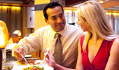 A man smiles while he takes a forkful of salad from his date's plate.