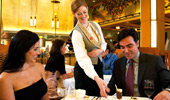 A server points to the bottom of a menu a man is holding while seated at the table.