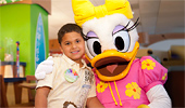 A brightly dressed Daisy Duck hugs a young Guest.