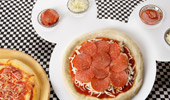 Fresh from the oven pizza and a pizza-in-the-process on a Mickey-shaped plate.