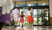 A mom and dad hold hands with their young girl who is dressed as Minnie Mouse.